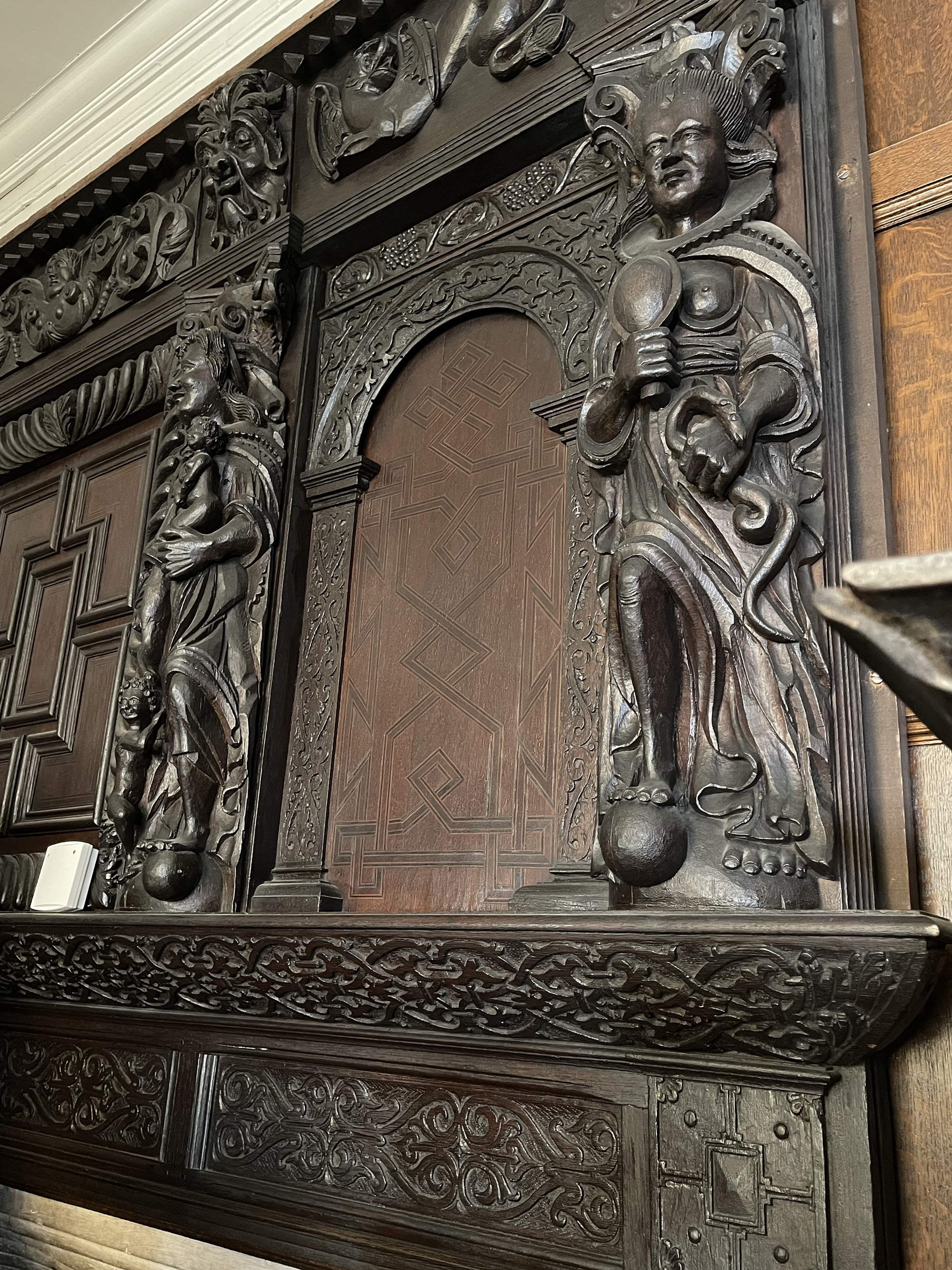 This grand carved wooden overmantel was salvaged in the early years of the 20th century from 32, Carr Street in Ipswich and is now on display in the Christchurch Mansion Museum. It has four large figures representing the virtues of Faith, Hope and Charity (the three theological virtues) along with ‘Prudence’, one of the four Cardinal Virtues (with Justice, Fortitude and Temperance). These female personifications are identified through the objects that they hold (their attributes). The ability to read these objects and correctly identify the nature of these allegorical figures was an essential part of the visual literacy of sixteenth and seventeenth century England. The Virtues were an ancient iconography that would have been familiar in late medieval church art. They continued to be depicted across the visual arts of early modern England, in tapestry and painted cloth, in print and in interior decoration.<br />
<br />
Here, viewers would know that the cross is the attribute of faith, the anchor represents Hope and that Charity nurses an infant. The mirror and snake held by Prudence, meanwhile, may be surprising to a modern audience given their association with vanity, and sin/the devil. In early modern understanding, however, the snake could symbolise wisdom and the mirror shows self-knowledge; taken together and in the context of the other Virtues the meaning of these symbols is clear. The Virtues were commonly depicted in large-scale domestic decoration where they represented the character and qualities of the upper middling householder; they would have been readily understood as such by all visitors to the house regardless of their ability to read or write.